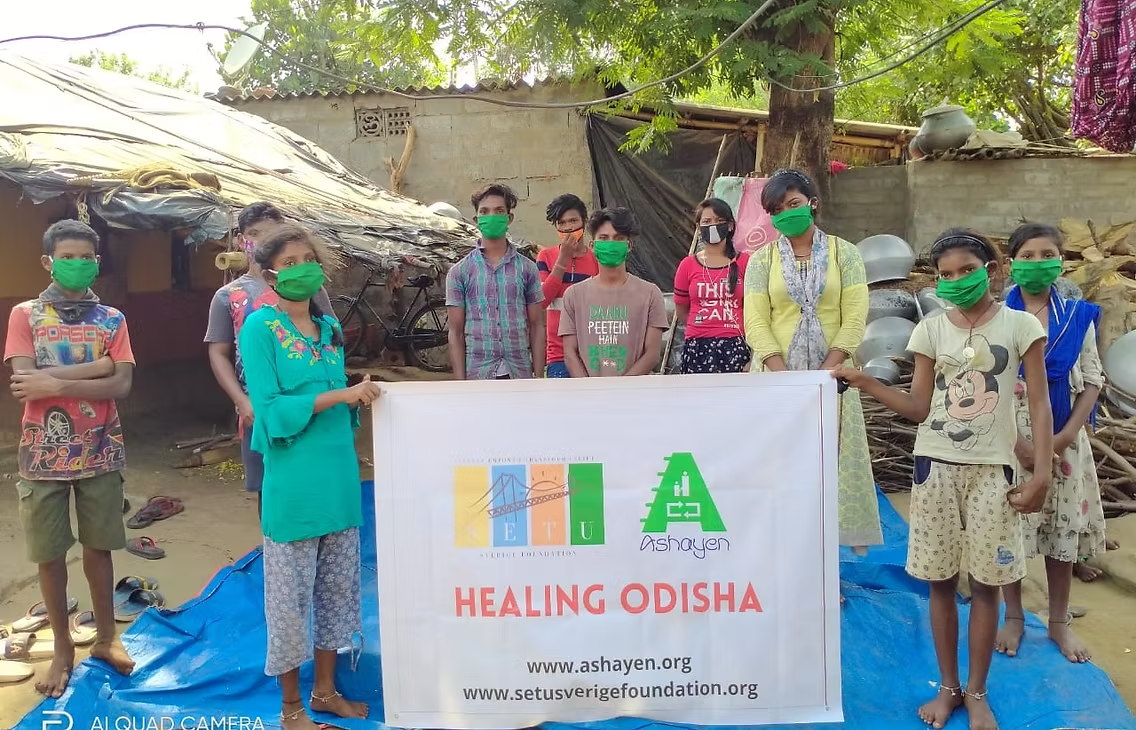 Young people wearing face masks holding a Healing Odisha banner from Setu Sverige Foundation and Ashayen in a village
