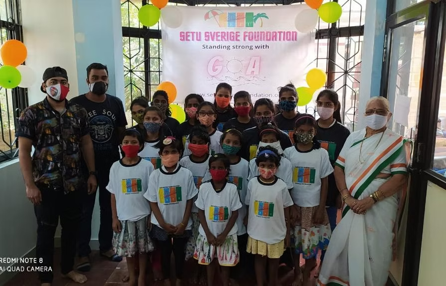 Children and volunteers gathered under a Setu Sverige Foundation banner at a Standing Strong with Goa event